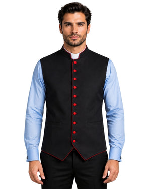 A man wearing a black waistcoat vest with red button and piping details, layered over a light blue dress shirt and black trousers, against a white background.