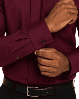 A close-up of a man's hands adjusting the cuff of a long-sleeve burgundy clerical shirt, paired with a black leather belt.