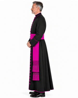 A man in profile wearing a Classic Clergy Cassock With Magenta Trim, a sash at the waist, and a matching pink front panel with tassel fringe, photographed against a plain white studio background.