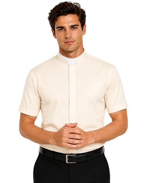 A man wearing a cream-colored short-sleeve clerical shirt with a white collar tab, paired with black trousers and a black belt, against a plain white background.