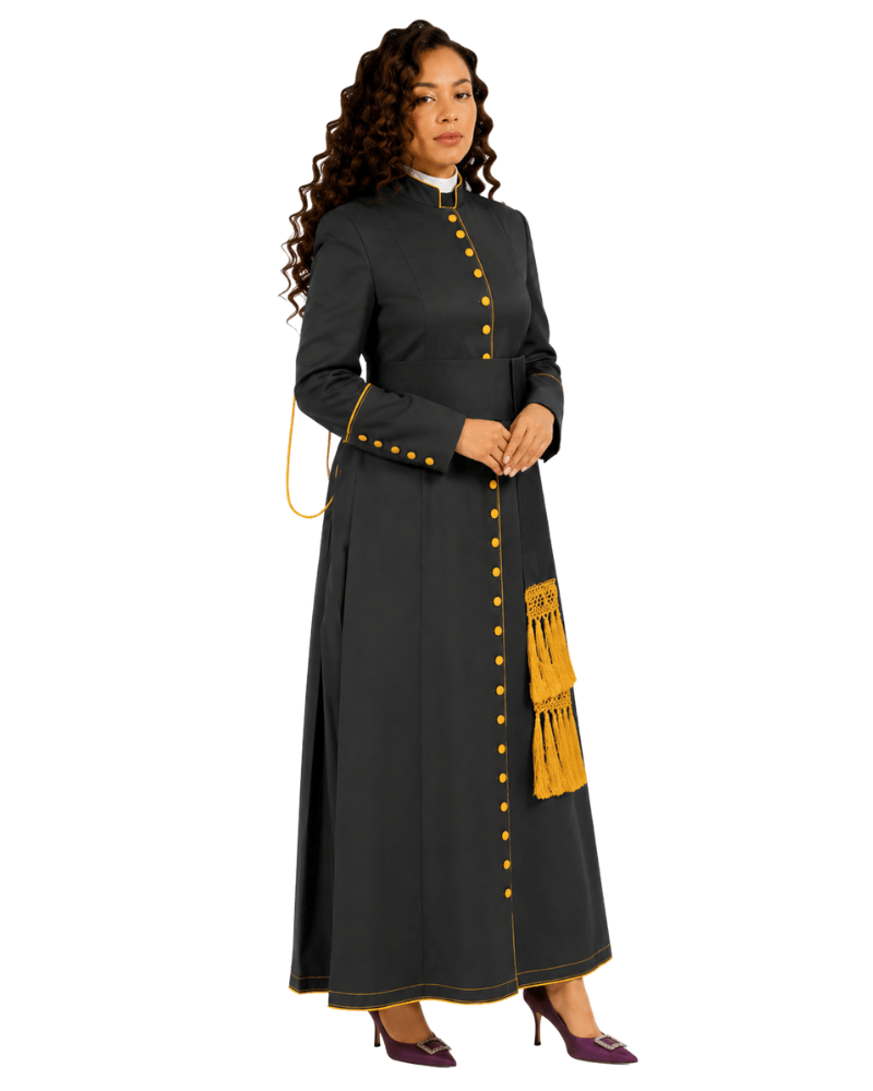 A woman modeling a long black cassock a gold fringe pocket, paired with purple heels against a white background.