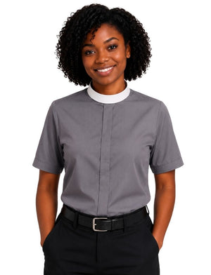 A smiling woman with curly black hair wearing a gray short-sleeve clerical shirt with a white mock neck collar, paired with black trousers and a black belt, against a plain white background.