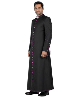 A man modeling a long black traditional Cassock with magenta button accents and trim, standing against a plain white background.
