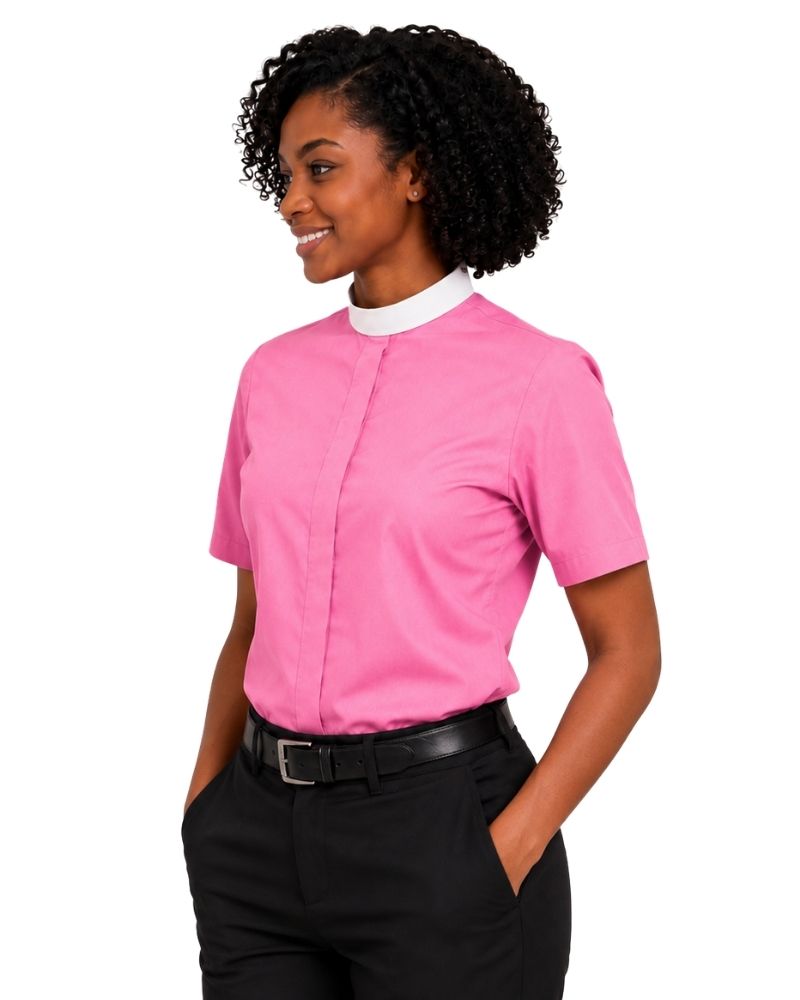 A woman wearing a bright pink short-sleeve clerical shirt with a contrasting white mock neck collar, paired with black trousers and a black belt, shown against a plain white background.