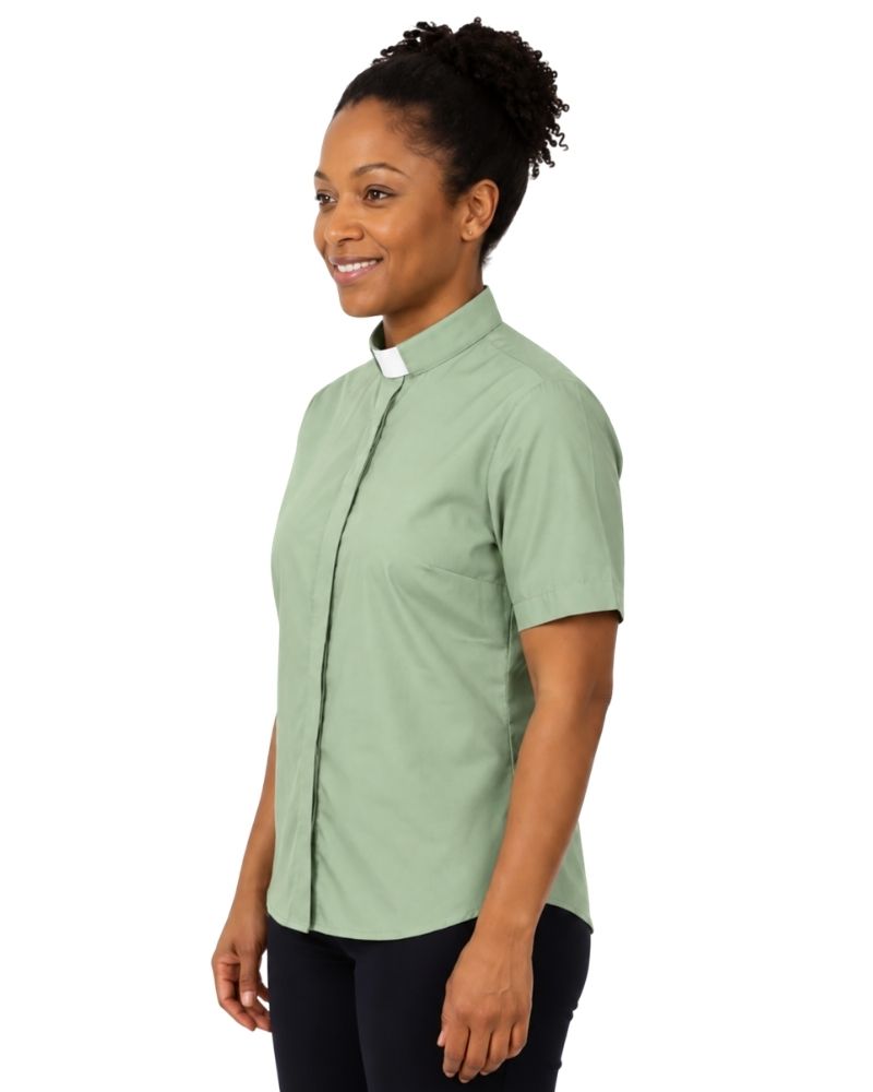 A woman wearing a light sage green short-sleeve clerical shirt with a white clerical collar, paired with dark pants, shown from a side profile against a plain white background.