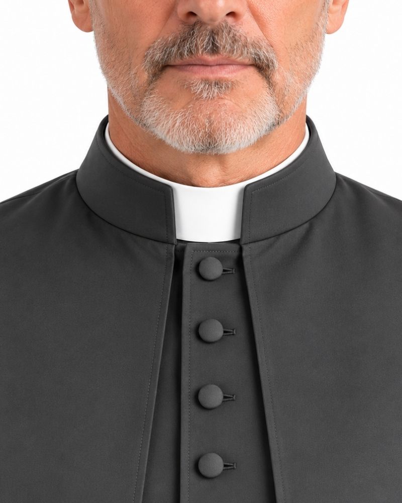 A close-up of a man wearing a Black Ethan Cassock with Shoulder Cape with a white clerical collar underneath, set against a plain white background.