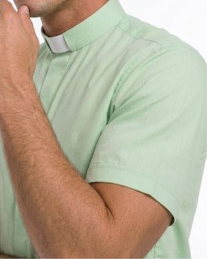 A close-up of a man wearing a light mint green short-sleeve clerical shirt with a white collar tab, against a plain white background.