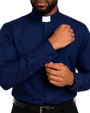 A man wearing a navy blue long-sleeve clerical shirt with a white clerical collar, adjusting the cuff with one hand while wearing a black belt.