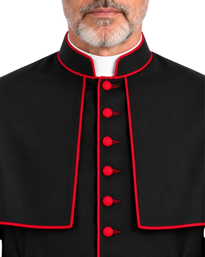 A close-up of a man wearing a black clerical cape with red piping and red decorative buttons, paired with a white collar, against a plain white background.
