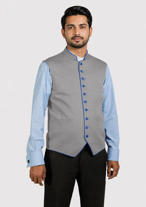Man wearing a gray vest over a light blue shirt with dark pants on a white background