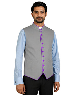 Man wearing a gray vest with purple buttons over a light blue shirt on a white background.