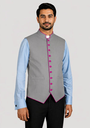 Man wearing a gray vest with pink buttons over a light blue shirt on a plain background