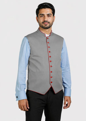Man wearing a gray vest with red buttons over a light blue shirt on a white background