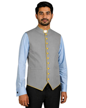 Man wearing a gray vest with yellow buttons over a light blue shirt on a white background.