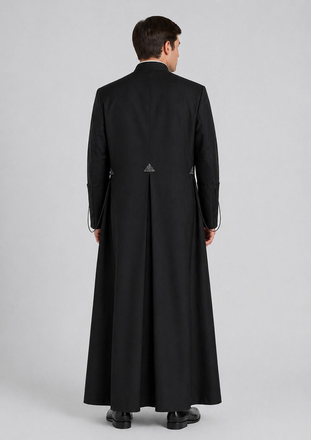 Man wearing a long black cassock on a gray background