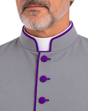 Close-up of a man wearing a Purple Abdiel Clergy Cassock with purple piping and matching purple buttons over a white collar, on a white background.