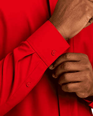 Close-up of a man wearing a bright red long-sleeve clerical shirt, adjusting the cuff with one hand while the other hand rests near the pocket.