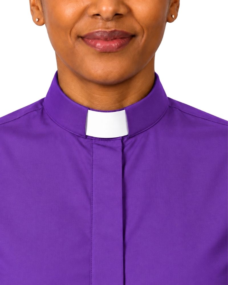 A close-up of a woman wearing a purple clerical shirt with a white collar, shown against a plain white background.