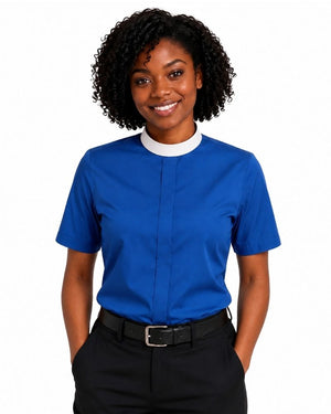 A smiling woman with curly black hair wearing a royal blue short-sleeve clerical shirt with a white mock neck trim, paired with black trousers and a black belt, against a plain white background.