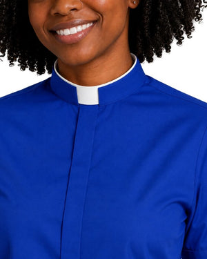 A close-up of a smiling woman wearing a royal blue clerical shirt with a white collar tab, set against a plain white background.