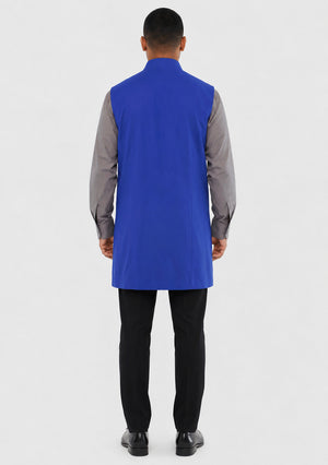 Man wearing a blue vest over a gray shirt with black pants on a white background
