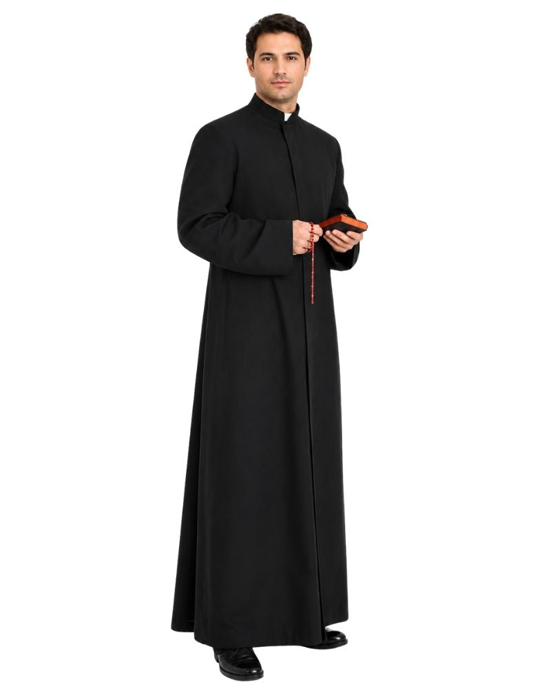 A man modeling a long-sleeved black clerical robe with a high collar, standing against a plain white background and holding a small red book and rosary.