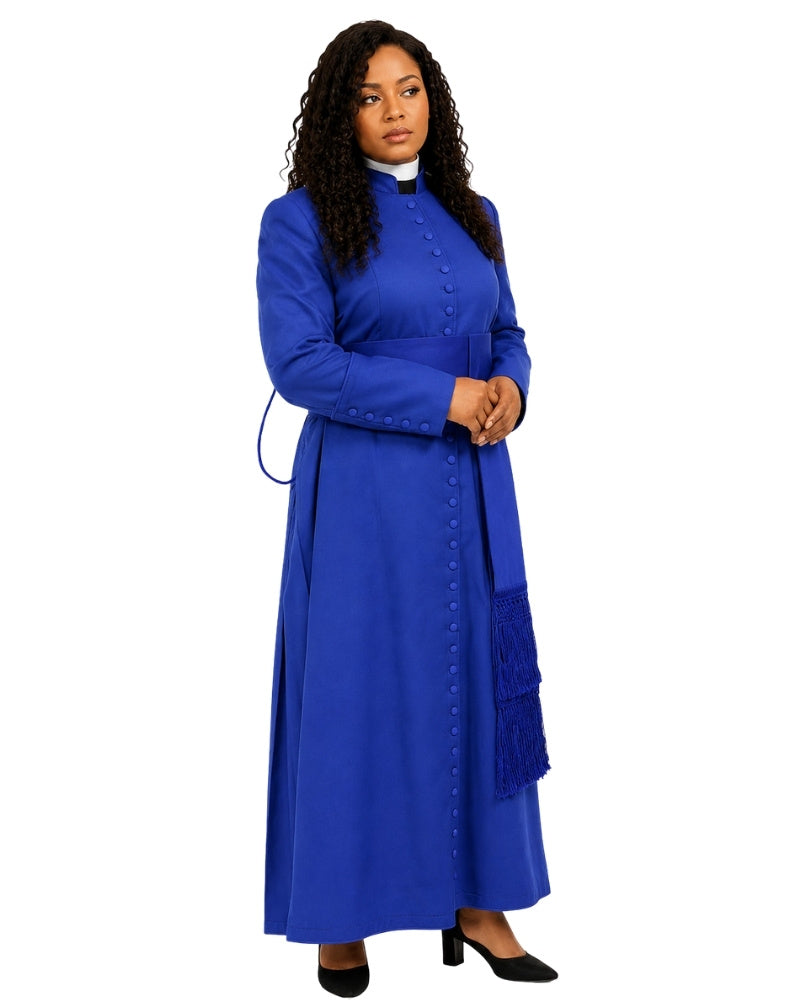 A woman modeling a long royal blue cassock with a high collar, front button closure, and fringe detail on the skirt, paired with black heels against a plain white background.