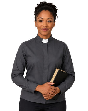 A woman wearing a dark gray long-sleeve clerical shirt with a white collar, holding a black book against a plain white background.