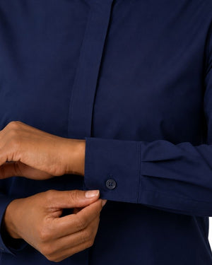 Close-up of a women hands adjusting the cuff of a navy blue long-sleeve clerical shirt.