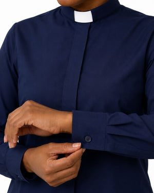A close-up of a women wearing a navy blue long-sleeve clerical shirt with a white collar and button cuffs, adjusting the cuff with both hands.