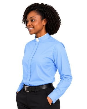 A woman with curly black hair wearing a light blue long-sleeve clerical shirt with a white collar, paired with black trousers and a black belt, shown against a plain white background.