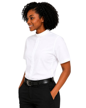 A woman with curly black hair wearing a white short-sleeve clerical shirt tucked into black trousers with a black belt, photographed against a plain white background.