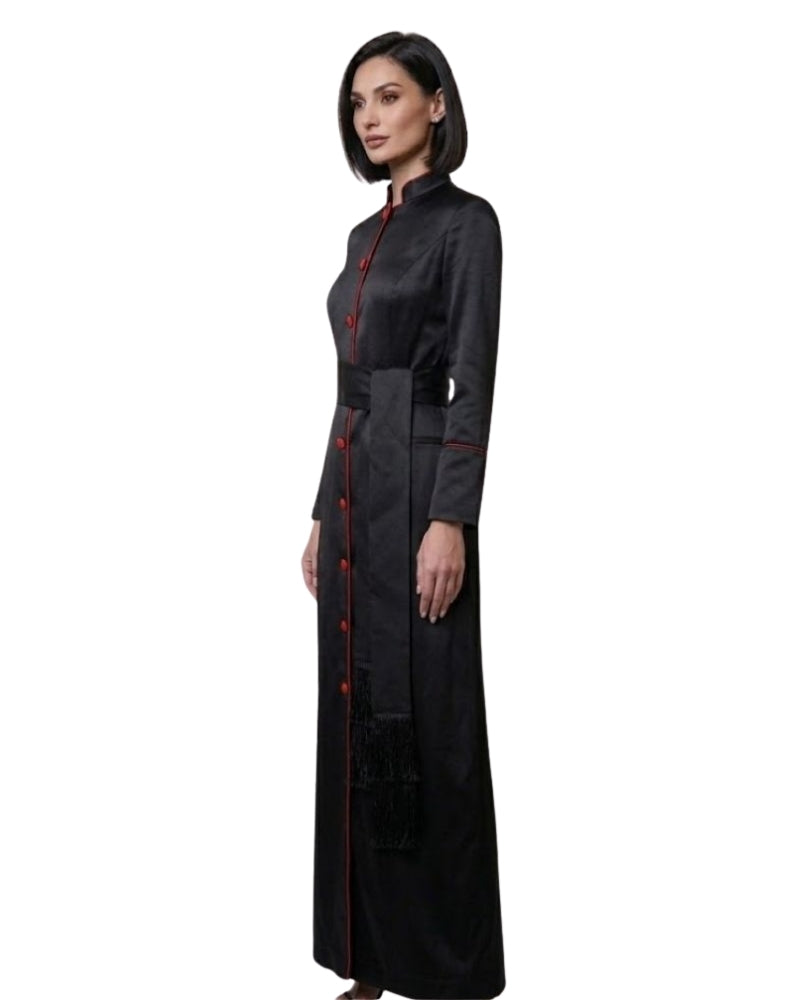 A woman modeling a long black robe with red trim and red buttons, shown in profile against a plain white background.