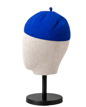 A clergy zucchetto cap with a vibrant blue top half and a light beige textured bottom half, displayed on a fabric mannequin head mounted on a black stand against a white background.