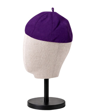 A clergy zucchetto cap with a purple top panel and a light beige lower panel, displayed on a fabric mannequin head mounted on a black stand against a white background.