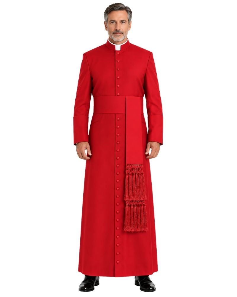 A man modeling a Advik Red Clergy Cassock with a high collar, front buttons, a waist belt, and a decorative tassel panel on the right side, paired with a white clerical collar and black dress shoes against a plain white background.
