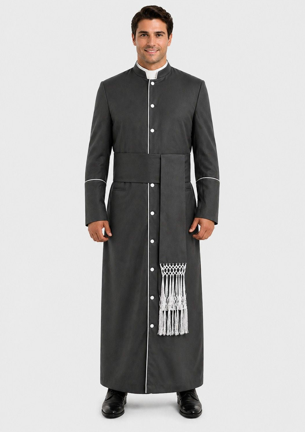 Man wearing a long black robe with white buttons and trim on a plain background