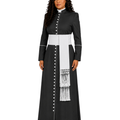 A woman modeling a long black cassock with a wide white waist sash, white vertical paneling, white decorative buttons, and a white fringed hanging detail, shown against a plain white background.