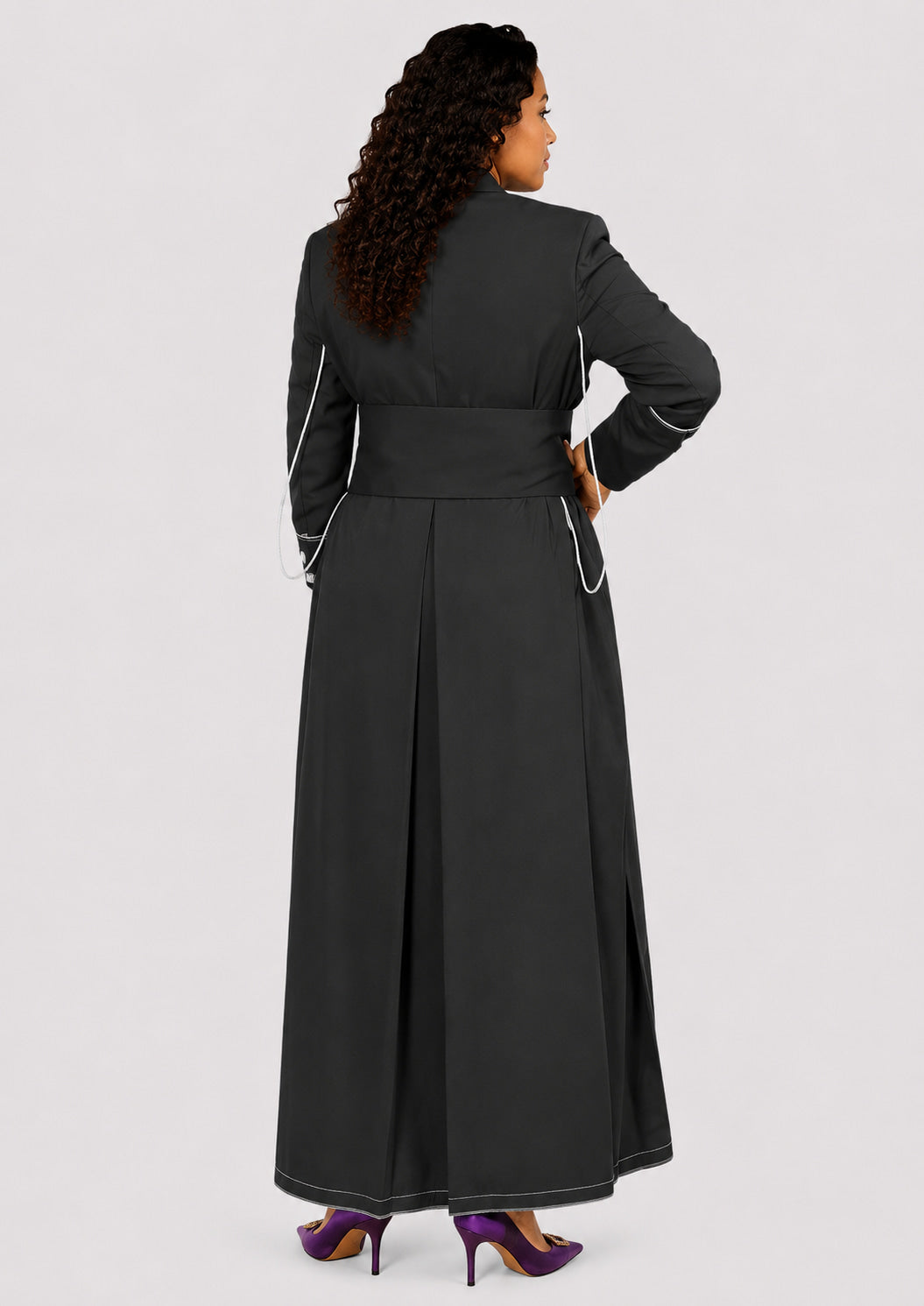 Woman wearing a long black robe with white piping on a light gray background