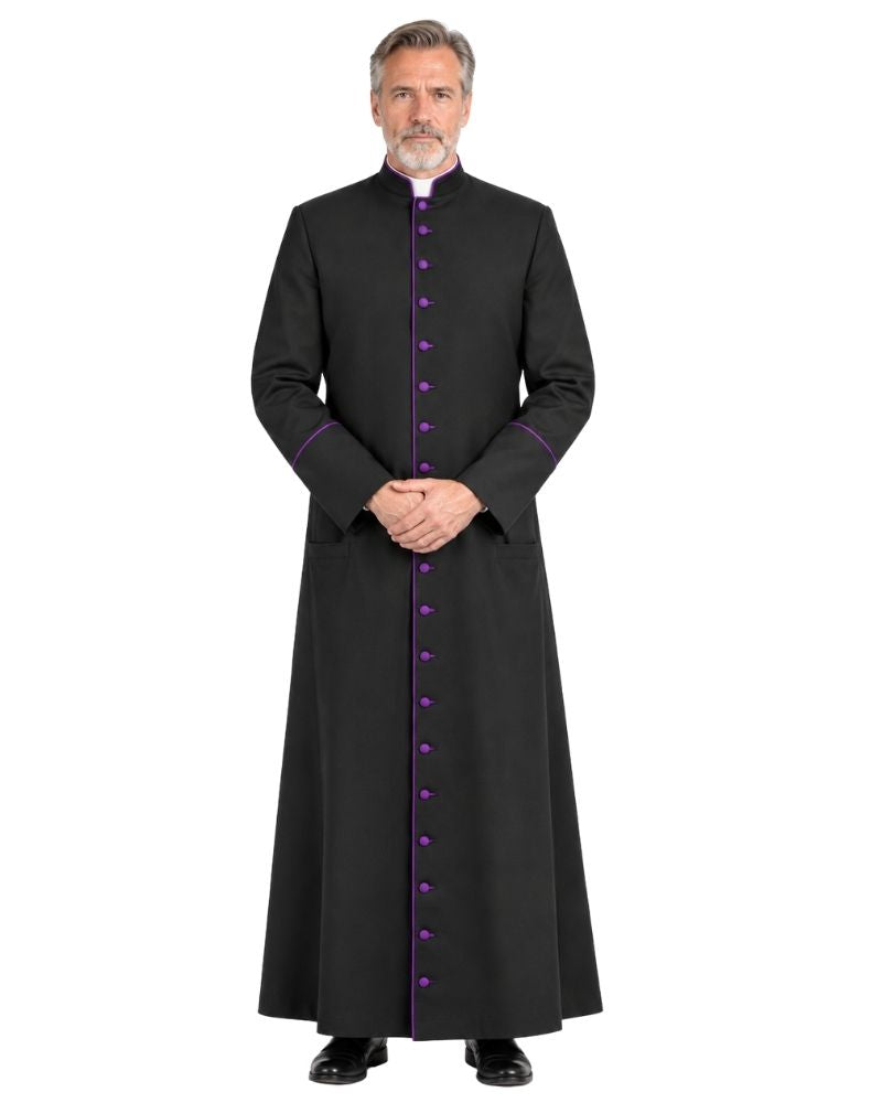 A man wearing a Black Clergy Cassock With Roman Purple Trim and purple buttons, standing against a plain white background.