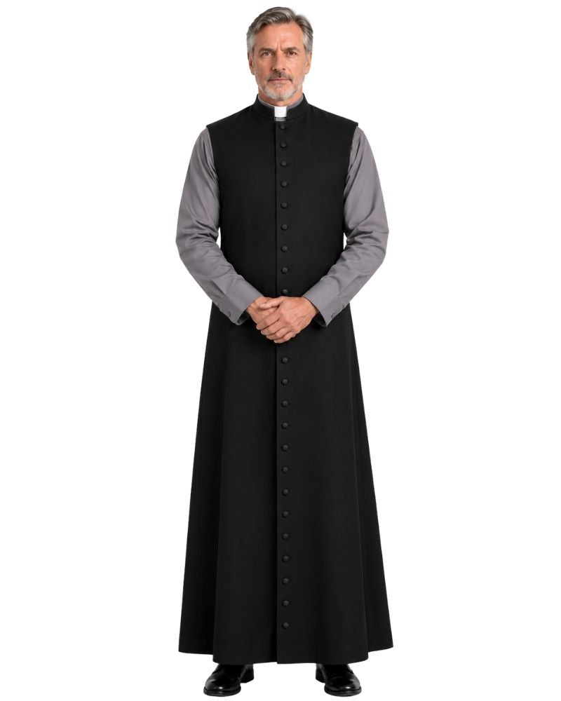A man modeling a Black Jedidiah Sleeveless Clergy Robe over a gray long-sleeve clerical shirt, with a white clerical collar and black dress shoes, against a plain white background.