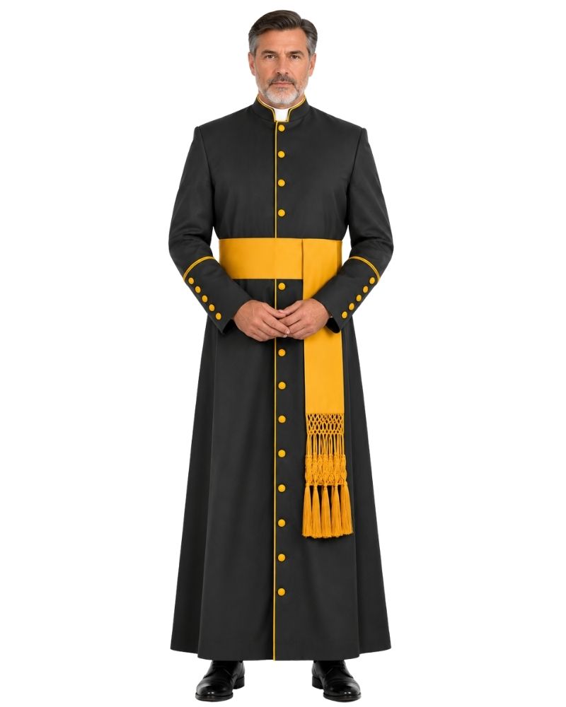 A man modeling a Black Roman Cassock With Yellow Trim with gold buttons, a yellow sash, and a matching yellow stole with fringe, against a plain white background.