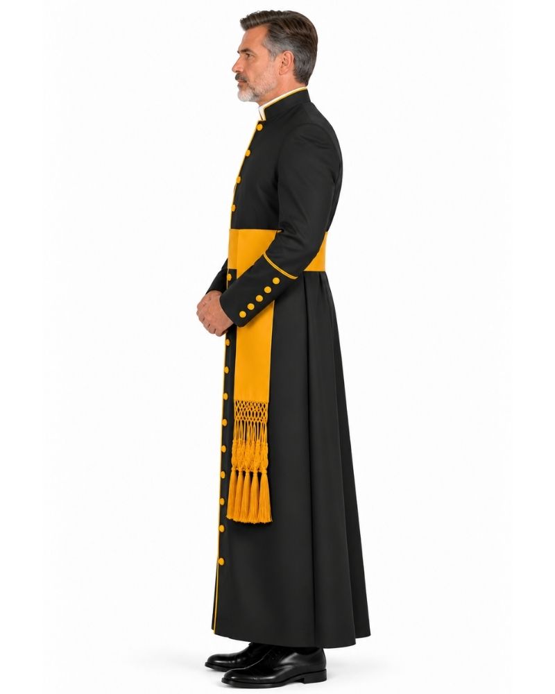 A man shown in profile wearing a Black Roman Cassock With Yellow Trim with bold yellow panels, yellow buttons, and a matching yellow sash with fringe, photographed against a plain white studio background.