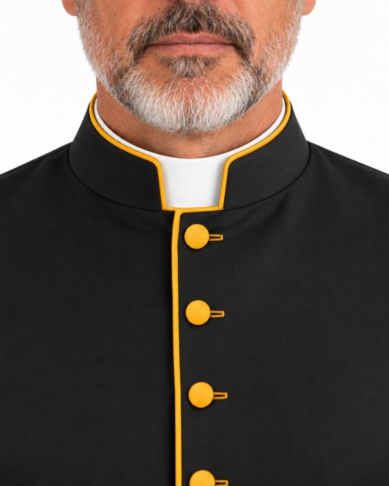 Close-up of a man wearing a Black Roman Cassock With Yellow Trim and yellow buttons over a white collar, cropped from the lower face to the chest on a white background.
