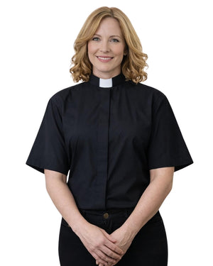 A woman with blonde hair wearing a black short-sleeve clerical shirt with a white collar, standing against a plain white background.