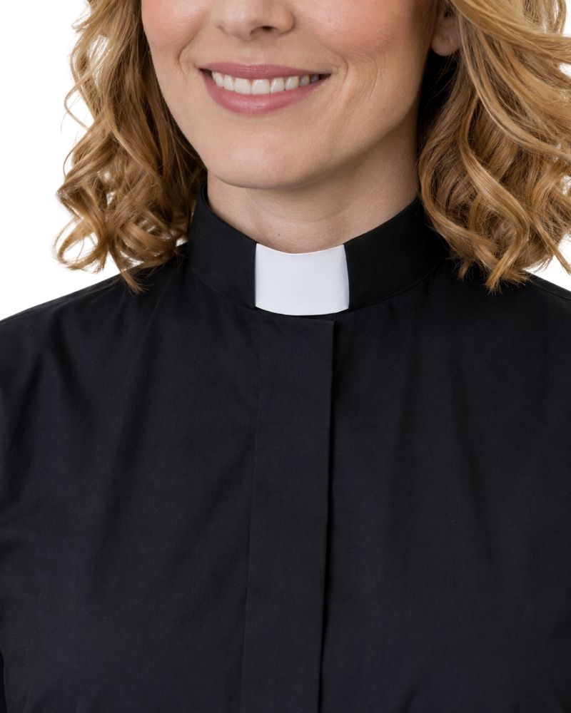 A close-up of a woman wearing a black clerical shirt with a white collar, shown from the chest up against a plain white background.