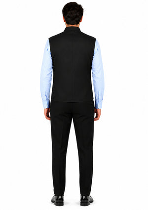Man wearing a black vest over a light blue shirt with black pants on a white background