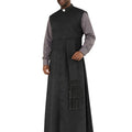 A man modeling a black priestly vestment set consisting of a long black surplice robe with a decorative tassel detail and a matching black button-front vest over a gray long-sleeve shirt, on a plain white background.