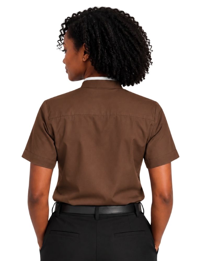 A woman with curly black hair wearing a brown short-sleeve clerical shirt with a white collar tab, paired with black trousers and a black belt, against a plain white background.