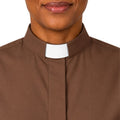 A close-up of a woman wearing a brown clerical shirt with a white collar, shown against a plain white background.